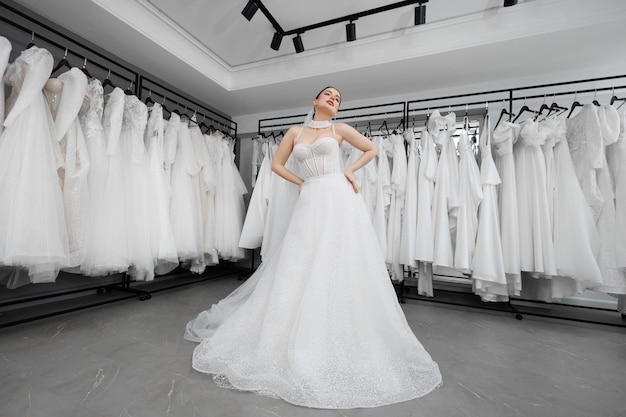 Foto a noiva tenta um vestido de noiva branco contra o fundo de um grande número de vestidos.