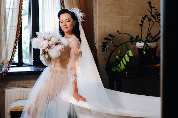 A noiva, vestida com um vestido boudoir transparente e calcinha, senta-se perto de uma banheira vintage com uma pena nas mãos, O dia da noiva.