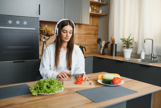 A nutricionista de blogueiras atléticas prepara uma salada com legumes frescos e realiza uma videoconferência sobre alimentação saudável no laptop na cozinha