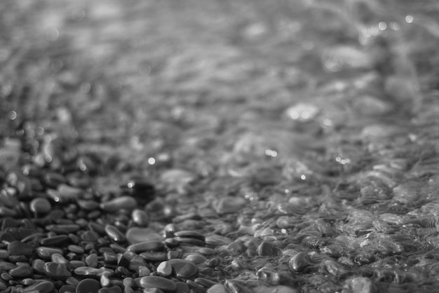 A onda do mar transparente clara rola em uma praia de seixos rochosos o conceito de férias e tranquilidade de viagem relaxamento e reflexão em um dia quente de verão closeup desfocagem de fundo preto e branco bokeh