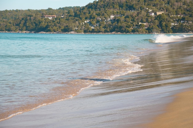 A onda do mar turquesa rola na costa plana e levemente inclinada da praia arenosa