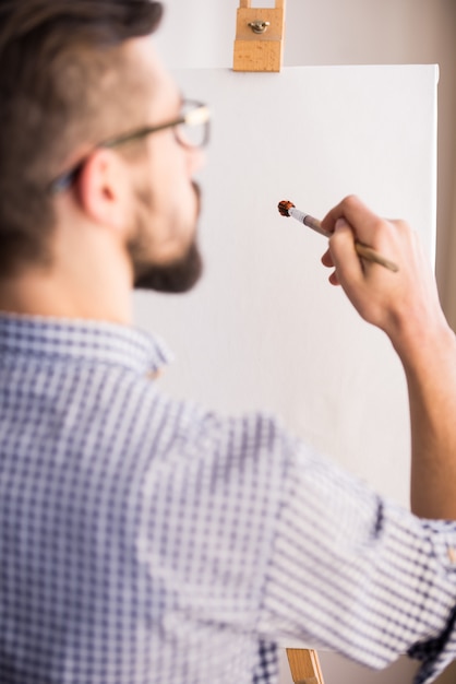 A opinião traseira o homem novo está pintando em uma lona vazia.