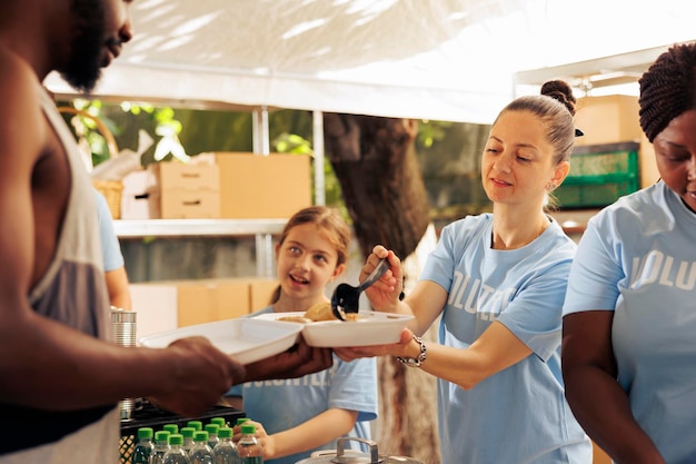 A organização humanitária recruta uma equipa diversificada para distribuir alimentos gratuitamente, apoiando pessoas menos privilegiadas e sem-abrigo, num esforço para aliviar a pobreza. Mulheres voluntárias alimentam homem afro-americano faminto.