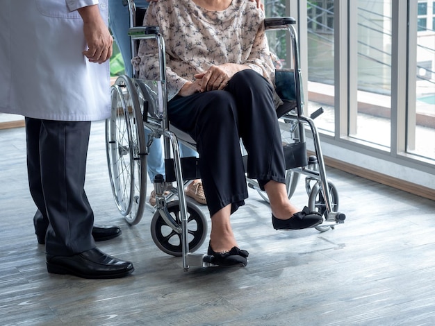 A paciente idosa senta-se em cadeira de rodas no chão enquanto o médico de jaleco branco fica ao lado para visitá-la dentro da sala de espera do hospital Cuidados de saúde e conceito médico