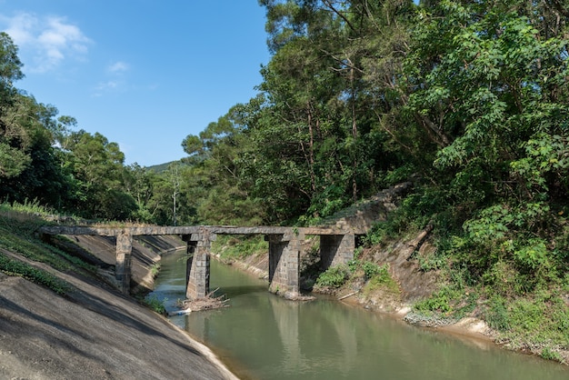 A paisagem ao lado do reservatório é de céu azul, nuvens brancas, montanhas verdes e águas claras