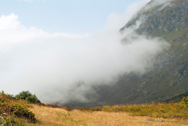 A paisagem das montanhas é uma nuvem rastejando no prado alpino outonal ao longo de uma encosta de montanha rochosa