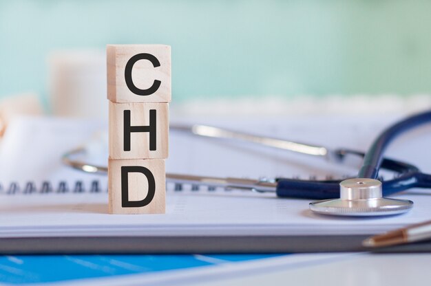 A palavra CHD é escrita em cubos de madeira perto de um estetoscópio sobre um fundo de papel. CHD - abreviação de doença cardíaca coronária. conceito médico