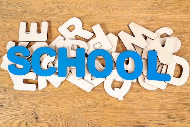 a palavra escola, disposta de letras azuis de madeira em uma pilha de letras diferentes sobre uma velha mesa de madeira