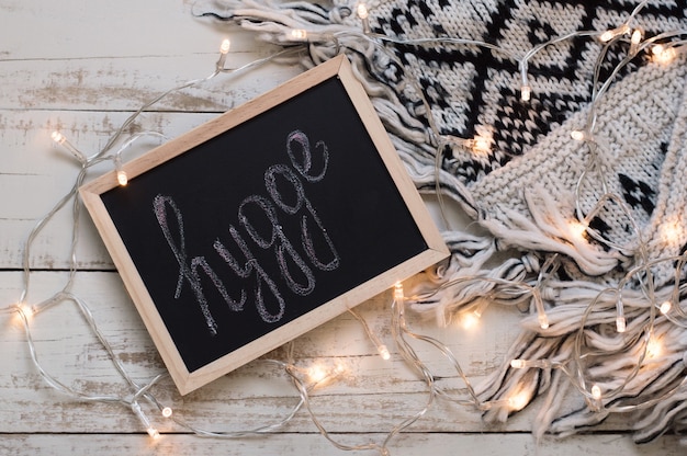 A palavra Hygge escrita em um cobertor de malha e luzes para a decoração da casa