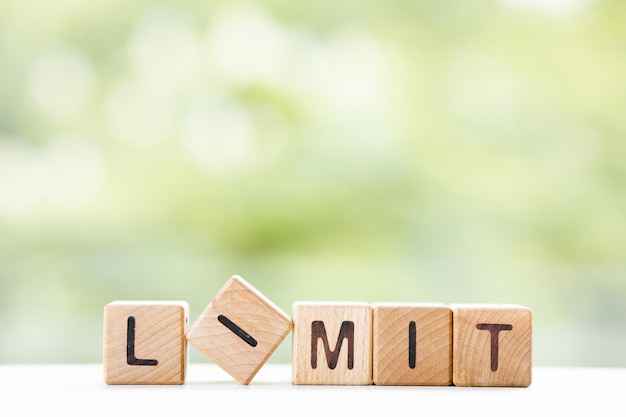 A palavra LIMIT está escrita em cubos de madeira em um fundo verde de verão Closeup de elementos de madeira