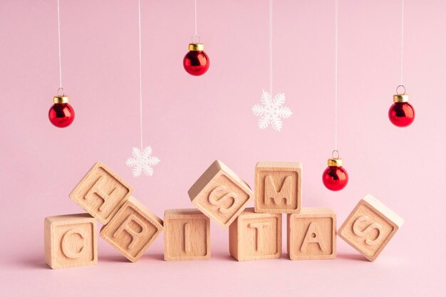 A palavra Natal composta de cubos de madeira em um fundo rosa Flocos de neve e bolas de Natal Cartão de Natal