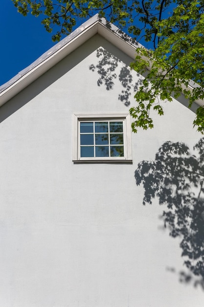 A parede branca vazia de uma casa velha de dois andares com um telhado de duas águas em um dia ensolarado de verão