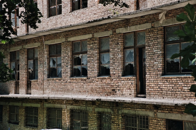 A parede de um antigo prédio de tijolos abandonado com janelas quebradas