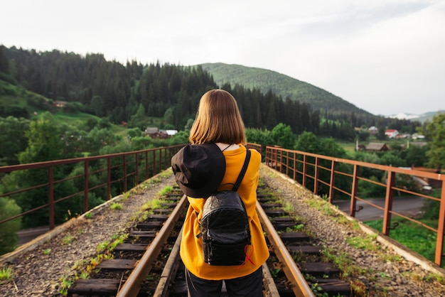 Foto a parte de trás de uma turista com uma mochila nas costas fica na pista da ponte ferroviária