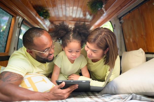 A parte de trás de uma van clássica branca, crianças brincam e aprendem sobre o mundo em seu tablet com os pais cuidando de ajudar