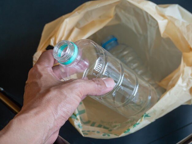 A parte do corpo da mão humana segurando uma garrafa de água está sendo jogada em um ambiente ecológico de plástico