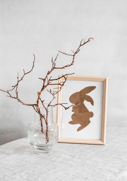 A páscoa ainda vive uma pintura caseira com um coelho de papel e galhos de árvores em um vaso de vidro em cima da mesa