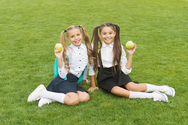 A pausa para a refeição pode ser divertida Crianças felizes seguram maçãs na grama verde Meninas aproveitam as férias escolares ao ar livre Alimentação e lanches saudáveis Intervalo para lanche natural Alimentação e nutrição Intervalo para o almoço