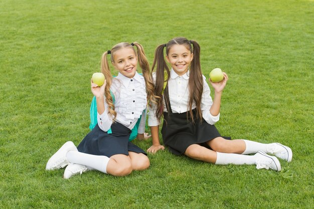 A pausa para a refeição pode ser divertida Crianças felizes seguram maçãs na grama verde Meninas aproveitam as férias escolares ao ar livre Alimentação e lanches saudáveis Intervalo para lanche natural Alimentação e nutrição Intervalo para o almoço