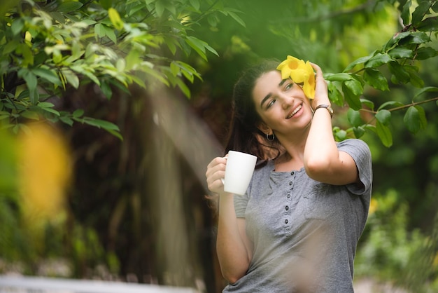 A pessoa jovem e bonita está feliz e desfruta com uma bebida de café pela manhã em casa relaxa o estilo de vida segurando uma xícara de café ou chá no parque ao ar livre da natureza sorria menina bonita com tempo de liberdade