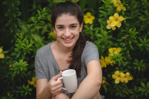 A pessoa jovem e bonita está feliz e desfruta com uma bebida de café pela manhã em casa relaxa o estilo de vida segurando uma xícara de café ou chá no parque ao ar livre da natureza sorria menina bonita com tempo de liberdade