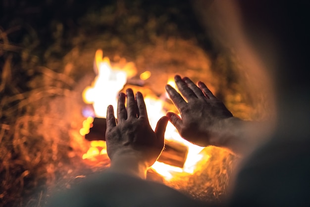 A pessoa que avisa as mãos perto da fogueira. noite noite