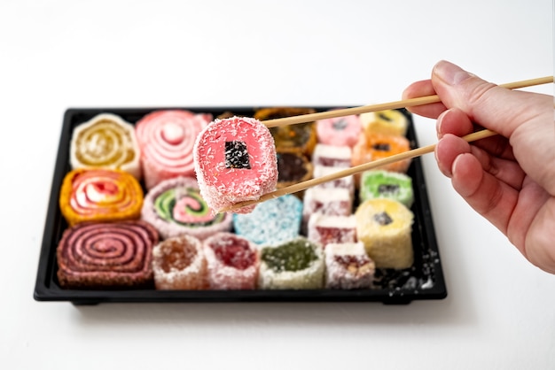 A pessoa segura um pedaço de um conjunto de balas de gelatina multicoloridas com pauzinhos