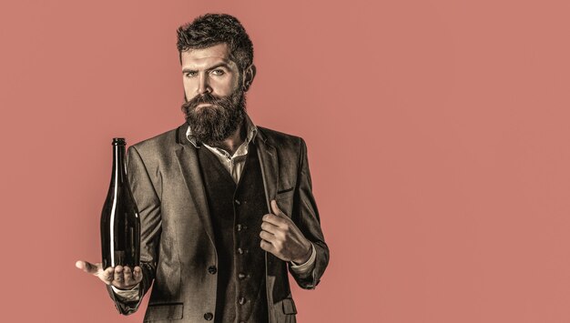 A pessoa segura uma garrafa de vinho tinto na mão. Homem segurando a garrafa com champanhe, vinho. Homem barbudo com uma garrafa de champanhe e uma taça.