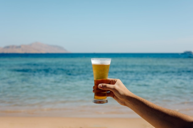 A pessoa segurando um copo de cerveja contra o fundo do mar