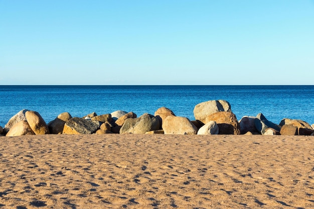 A praia arenosa e grandes pedregulhos em terra perto da água e a linha do horizonte sobre a água