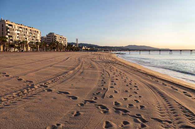 A praia de badalona ao nascer do sol com pegadas e vestígios de carro na areia