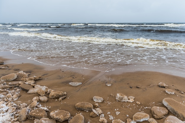 A praia de inverno do mar báltico tem neve e ondas fortes no mar