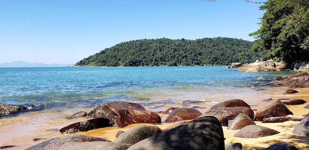 A praia vista da areia atrás de rochas com lodo que contrasta com um lindo céu azul