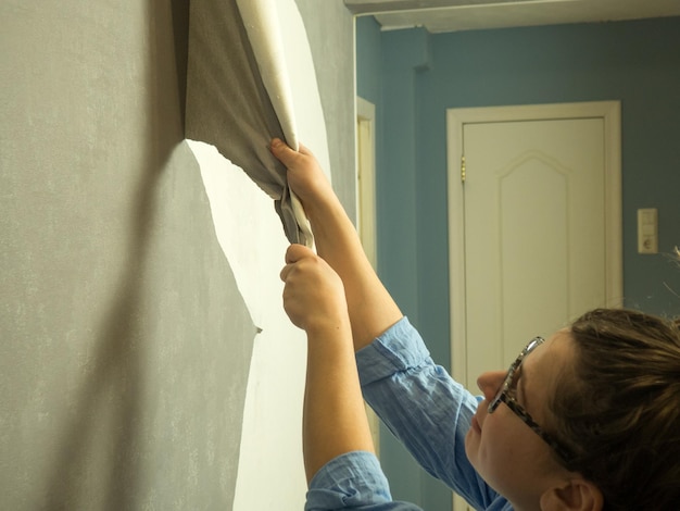 A rapariga arranca o papel de parede velho e faz renovações no apartamento.