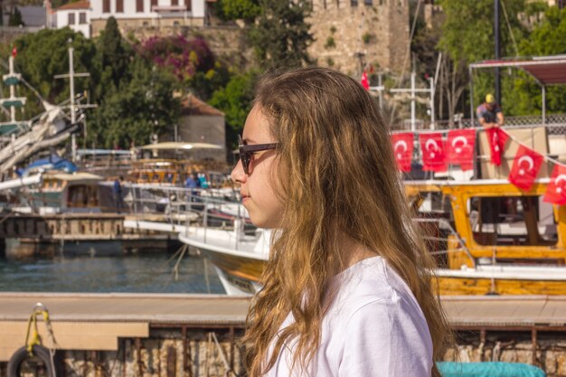 A rapariga com cabelo longo senta-se no cais na porta do iate e olha o mar azul