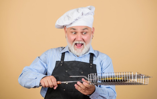 A receita requer muitos utensílios de cozinha amorosos para churrasco ele prefere comida grelhada Piquenique e churrasco Regras da cozinha jantar para a família Fim de semana em família homem feliz com chapéu de chef cozinhar homens com barba