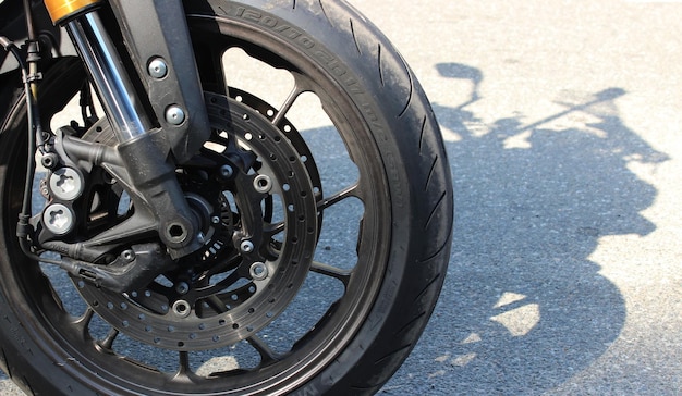 A roda dianteira de uma motocicleta de pé na beira da estrada e sua sombra no asfalto.