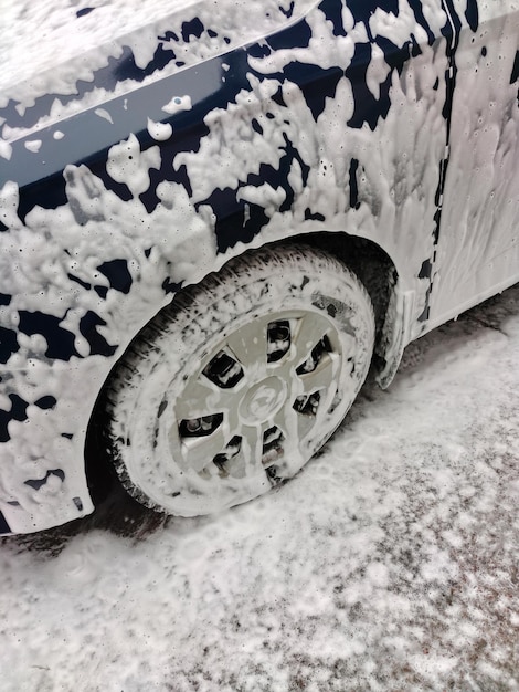 A roda e parte do carro estão cobertas de espuma branca no lava-rápido