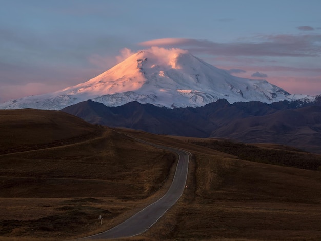 A rota para o amanhecer elbrus amanhecer majestoso rosa sobre o monte elbrus picos nevados ao amanhecer pôr do sol em tons de magenta paisagem atmosférica roxa com um vale de montanha nevada de alta altitude