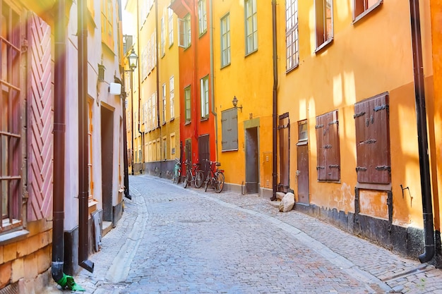 A rua estreita de paralelepípedos com uma bicicleta e casas medievais vermelhas amarelas do centro velho histórico de Gamla Stan de Estocolmo em dia ensolarado de verão.