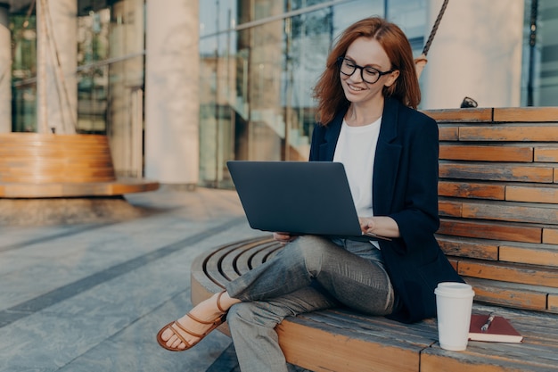 A ruiva inteligente navega em um laptop ao ar livre e faz projetos on-line