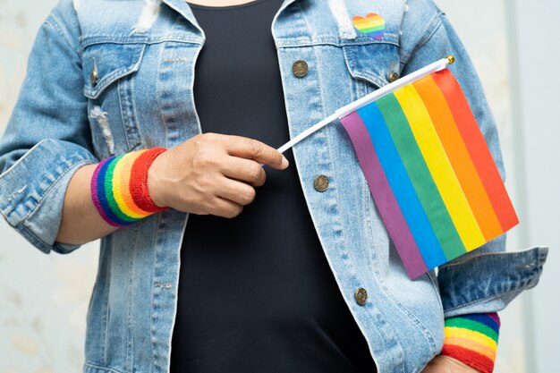 A senhora asiática que guarda a bandeira da cor do arco-íris, símbolo do mês do orgulho de LGBT comemora anual em junho.