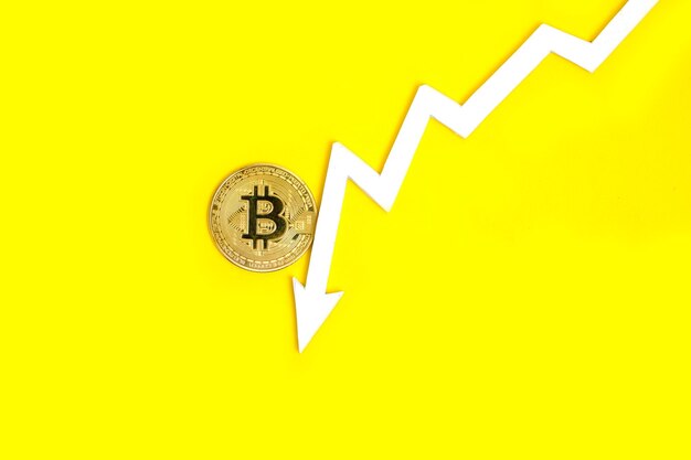 A seta do gráfico indica a queda e o colapso do valor da criptomoeda bitcoin fundo amarelo