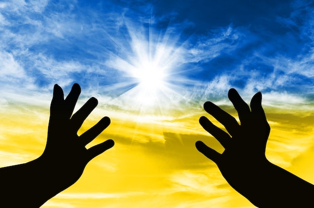 A silhueta das mãos virou-se para o céu com uma oração para a Ucrânia no contexto do céu na forma da bandeira ucraniana Conceito de crise e guerra na Ucrânia com a Rússia