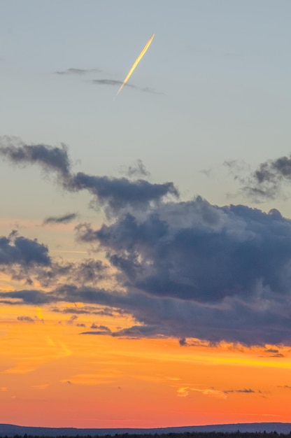 A silhueta de um avião de passageiros com um rastro nas nuvens iluminadas por um pôr do sol brilhante