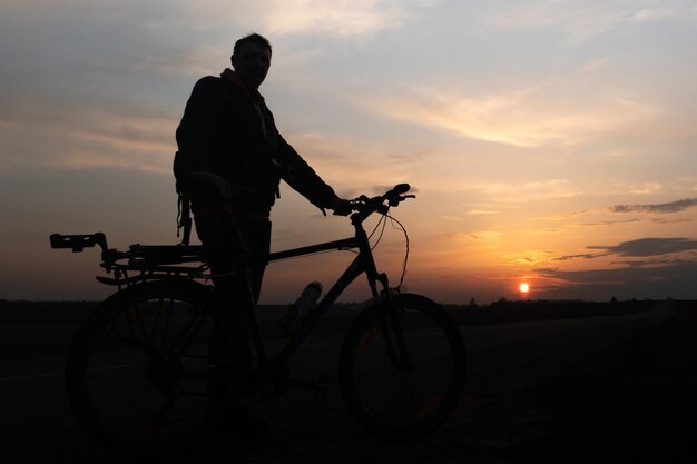 A silhueta de um ciclista no contexto do sol e o lindo céu O contorno de um homem ao lado de sua bicicleta no contexto do pôr do sol