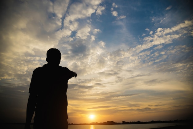 A silhueta de um homem com as mãos aponta para o céu por do sol.