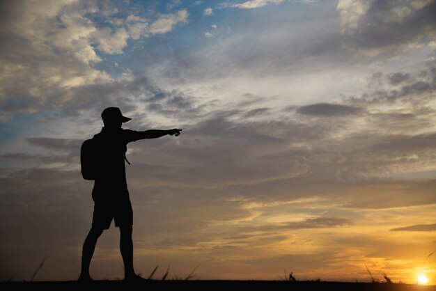 A silhueta de um homem com as mãos aponta para o céu por do sol.