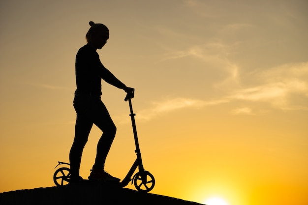 A silhueta de um homem de pé, segurando a scooter com um lindo nascer do sol