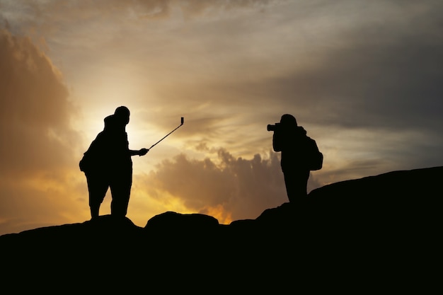 a silhueta dos womem e do homem toma a fotografia e o selfie com a montanha no por do sol.